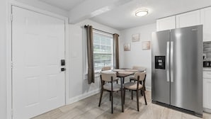 A compact kitchen with a dining table, chairs, a refrigerator, and a window with curtains. - Clearwater Top Floor #4 (Clearwater)