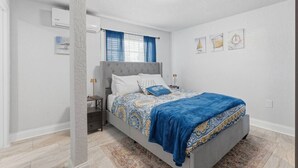 A bedroom with a bed, nightstand, and wall-mounted air conditioning unit. - Clearwater Top Floor #4 (Clearwater)