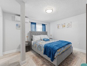 Un dormitorio con cama, mesita de noche y aire acondicionado de pared.