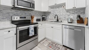 Una cocina moderna con armarios blancos, electrodomésticos de acero inoxidable, microondas, horno y lavavajillas.