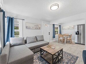 A modern living room with a grey sofa, a wooden coffee table, and a dining area with a table and chairs. - Clearwater Top floor #5 (Clearwater)