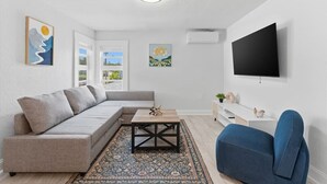 En moderne stue med en hjørnesofa, et sofabord, en blå lænestol, et fladskærms-tv og kunst på væggene.