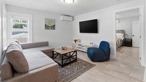 En moderne stue med sofa, sofabord, blå lænestol, fladskærms-tv og et tæppe med mønster.