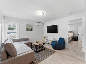 A modern living room with a sofa, a coffee table, a blue armchair, a flat-screen TV, and a patterned rug. - Clearwater Top Floor #3 (Clearwater)