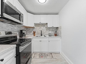 A kitchen with white cabinets, a black stove, a microwave, and a patterned backsplash. - Clearwater First Floor #2 (Clearwater)
