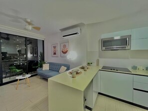 A modern kitchen with a central island, a dining area with a blue sofa, and a view through a glass door. - Modern Apartments PH Living 73 SF (Panama City)