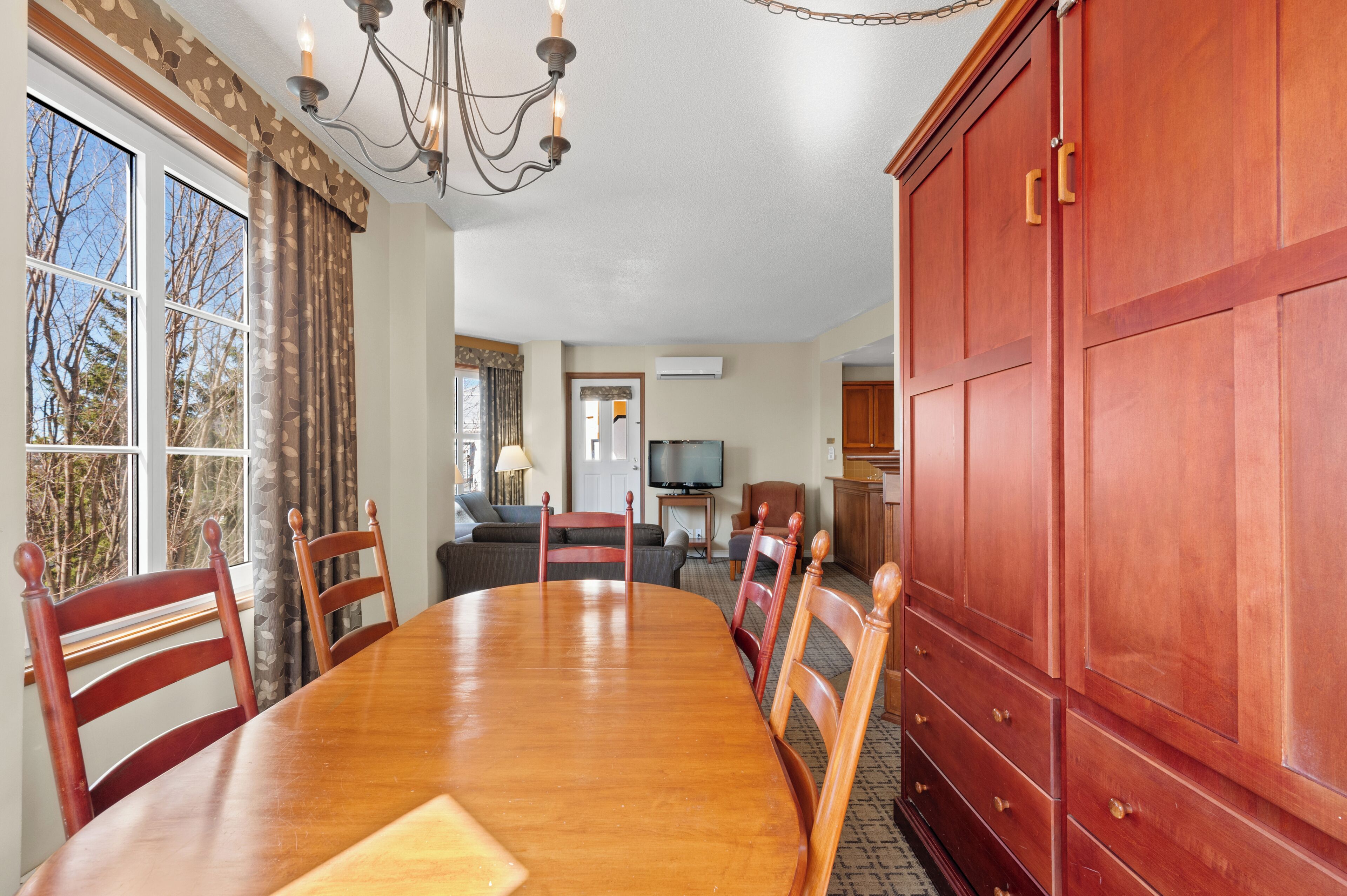 A dining area with a wooden table, chairs, a chandelier, and a large red cabinet.