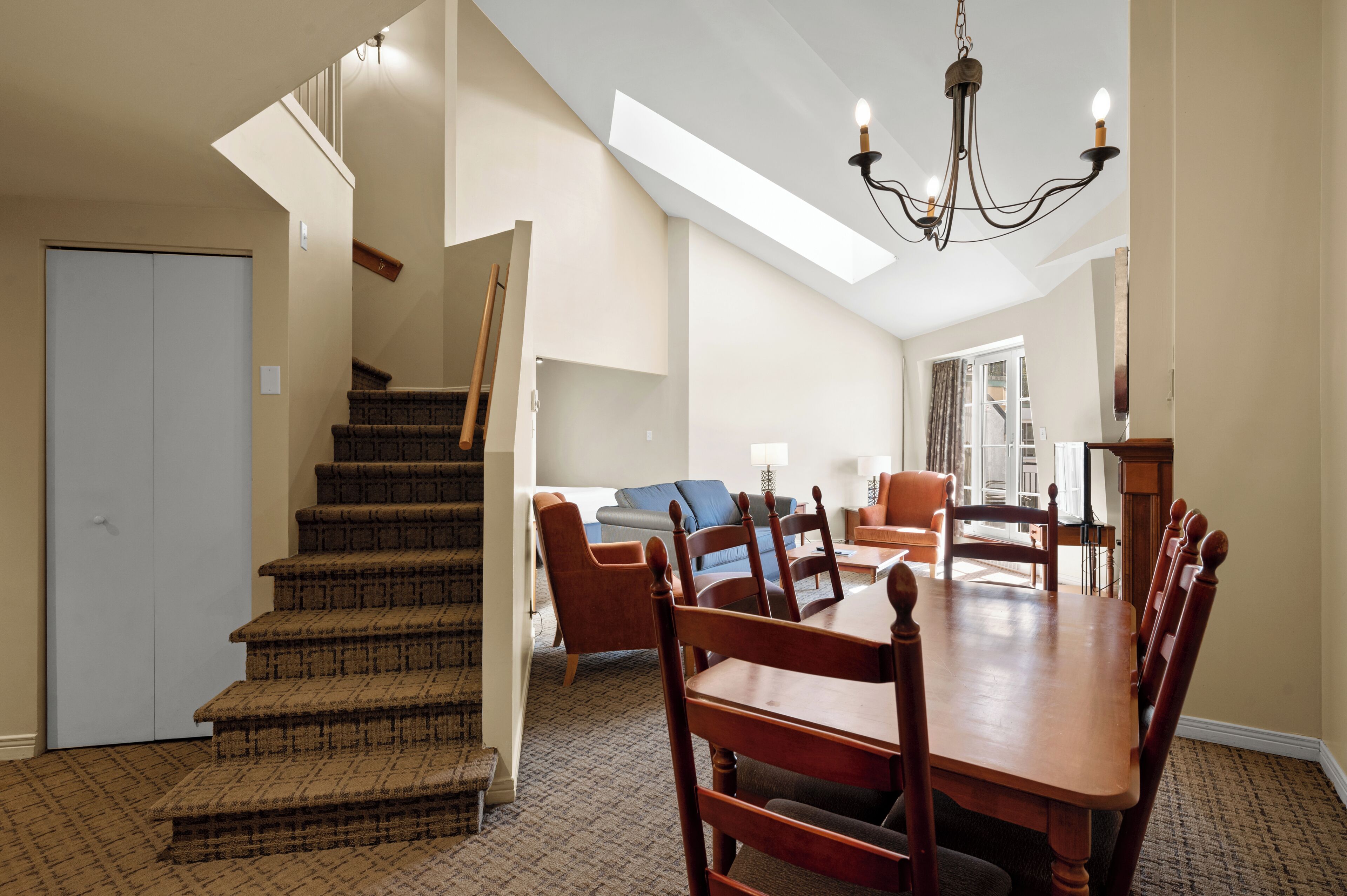 A dining area with a wooden table and chairs, a staircase, and a view of the outdoors.