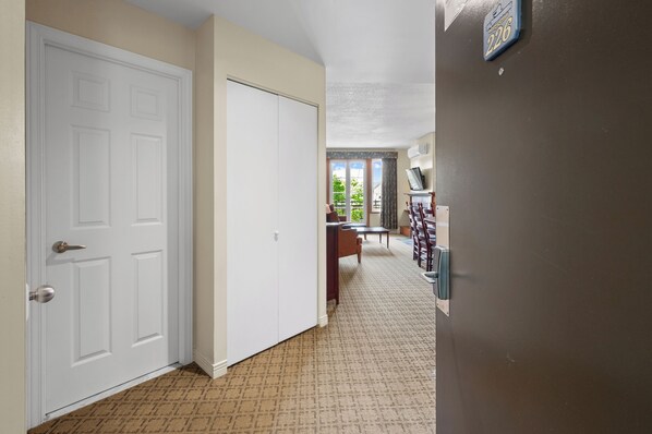 A hallway with a white door, a brown carpet, a dining area with a table and chairs, and a view through a window. - Le Johannsen by RVMT (Mont-Tremblant)