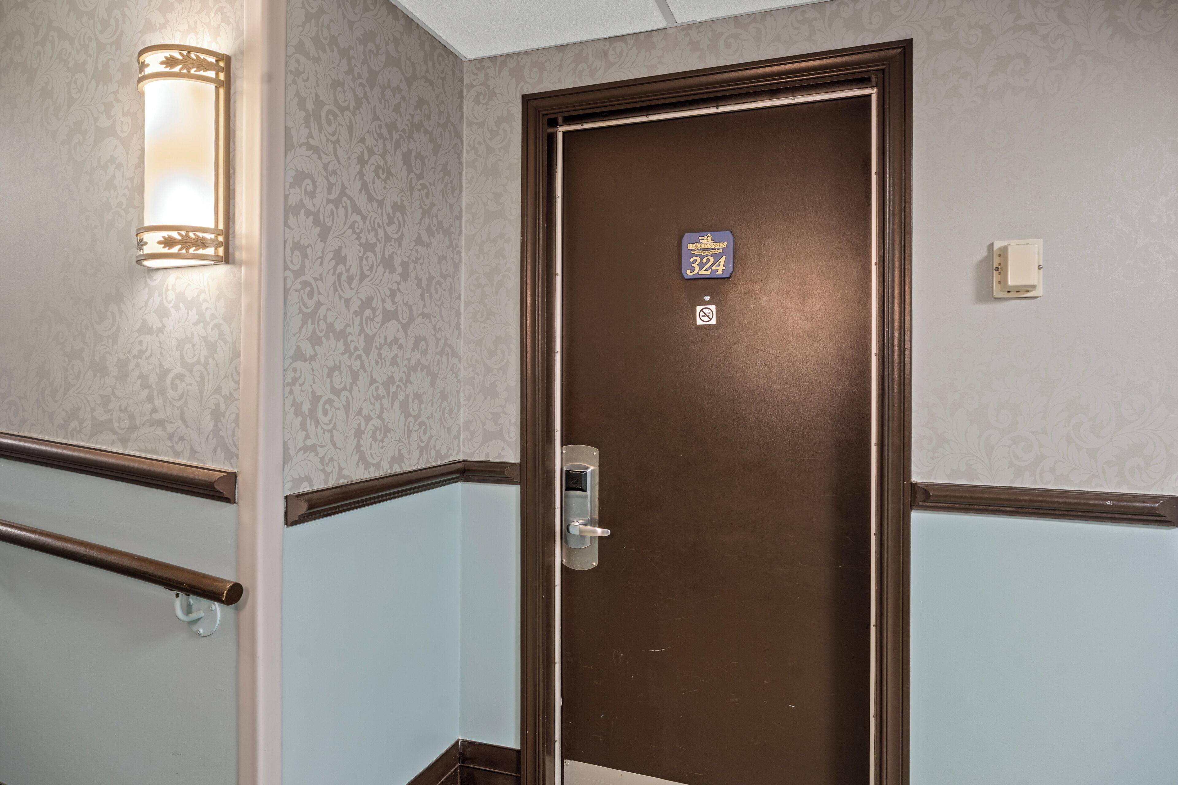 A hotel room door with a number sign, a light fixture, and a wall with a patterned design.