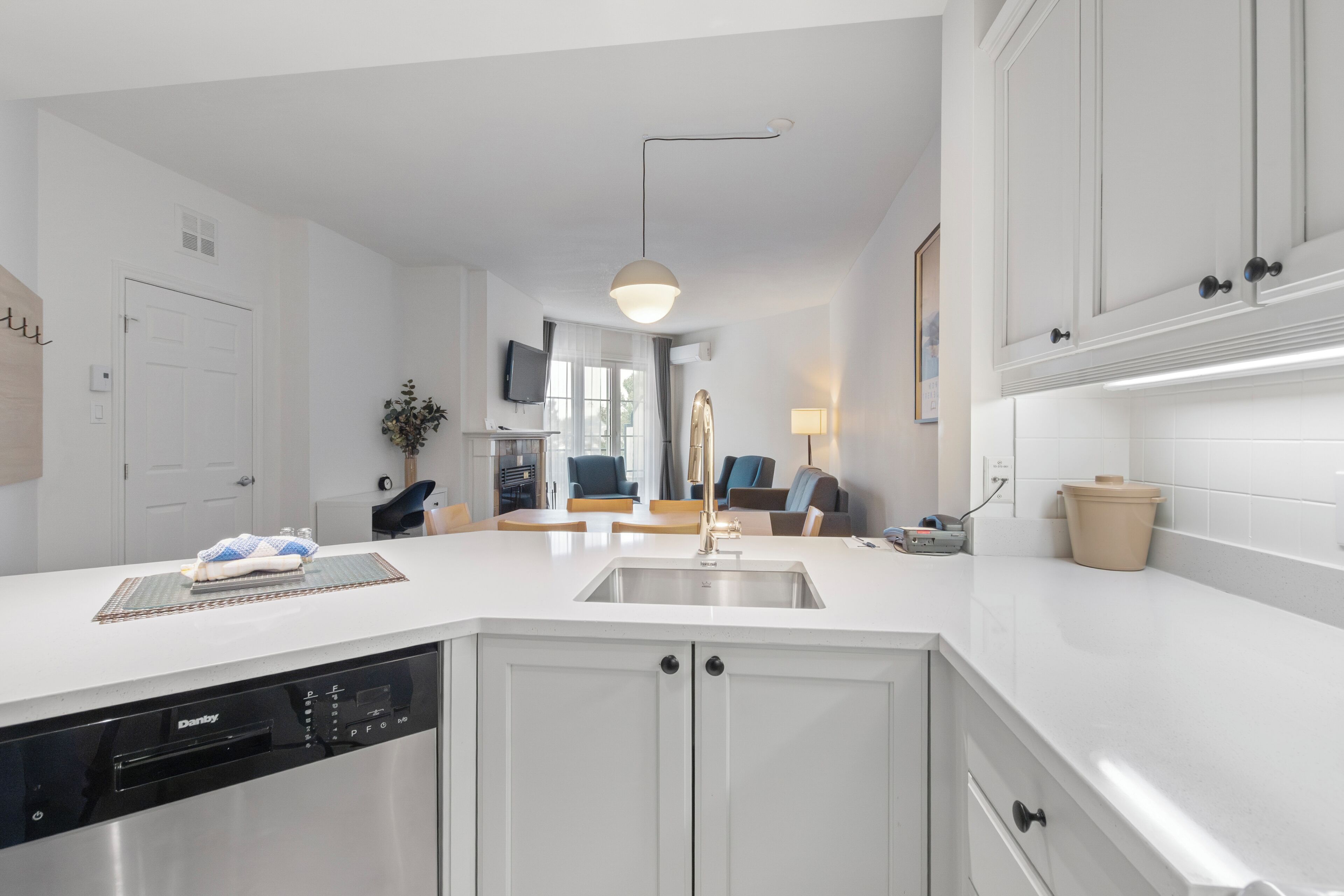 A modern kitchen with white cabinetry, a dishwasher, and a dining area with a table and chairs.