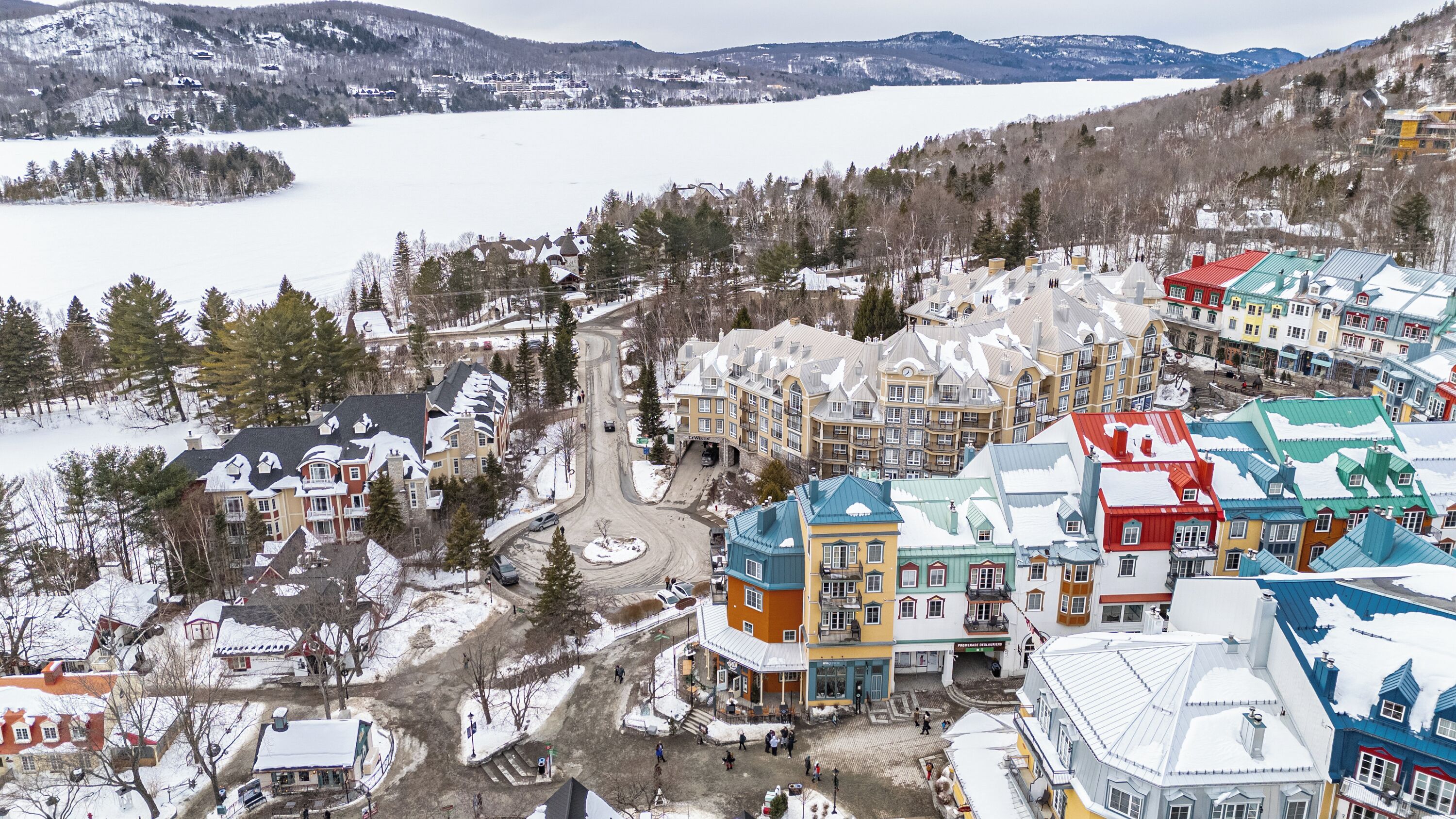 A snow-covered town with colorful buildings, a road, and a lake in the background.