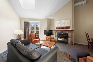 Una sala de estar con sofá, sillón, mesa de centro, chimenea, televisor y vistas por una ventana.