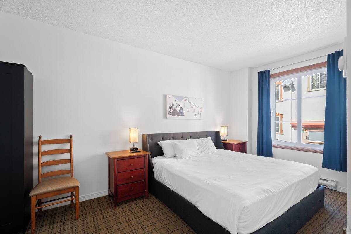 Una habitación de hotel con cama, una silla, una mesita de noche y un cuadro colgado en la pared.
