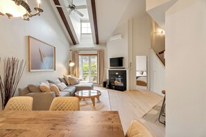 A spacious living room with a fireplace, a sofa set, a dining table, and a ceiling fan. - Le Johannsen by RVMT (Mont-Tremblant)