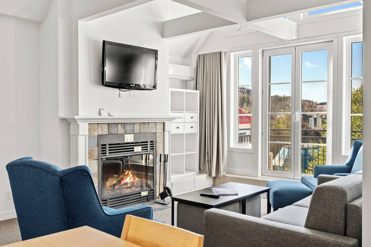Una sala de estar moderna con chimenea, asientos cómodos, un televisor de pantalla plana y ventanas grandes que ofrecen vistas al exterior.