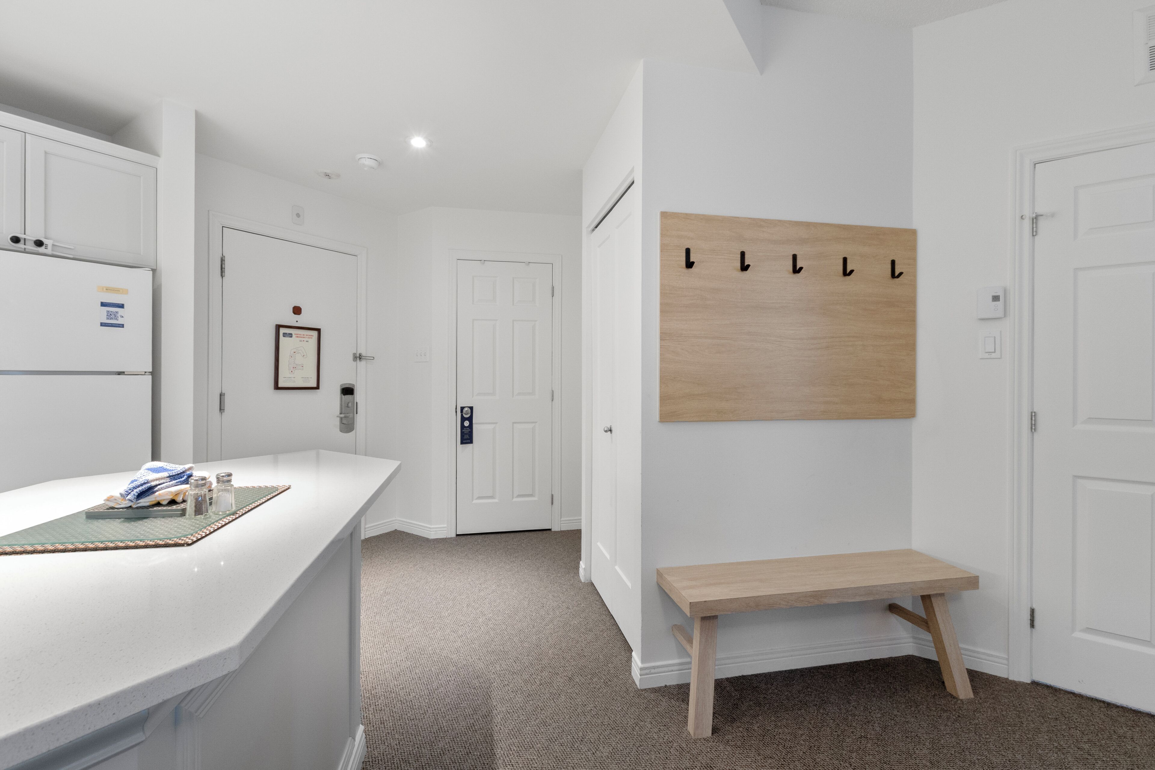 Un intérieur épuré et moderne, avec un comptoir blanc, un banc en bois et un porte-manteau fixé au mur.