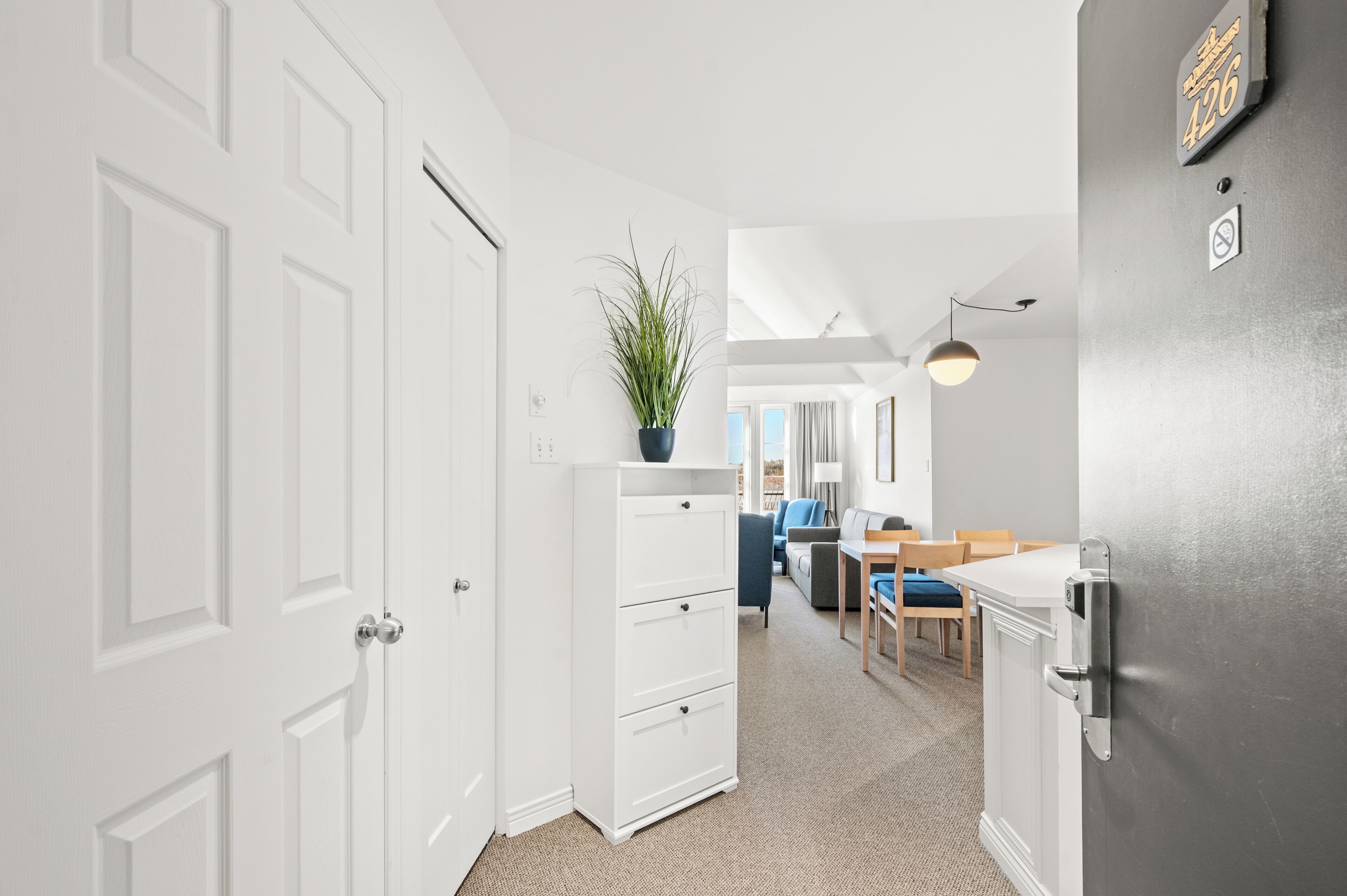 A modern kitchen with white cabinetry, a dining area with a table and chairs, and a hallway with a white door.