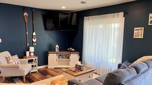 Un salon comprenant un canapé, un fauteuil, un téléviseur et un meuble contenant des objets décoratifs.