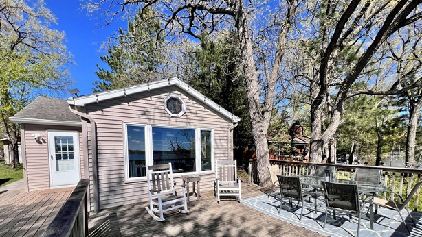 Une terrasse en bois avec un petit bâtiment, des sièges extérieurs et une vue sur des arbres et un lac.
