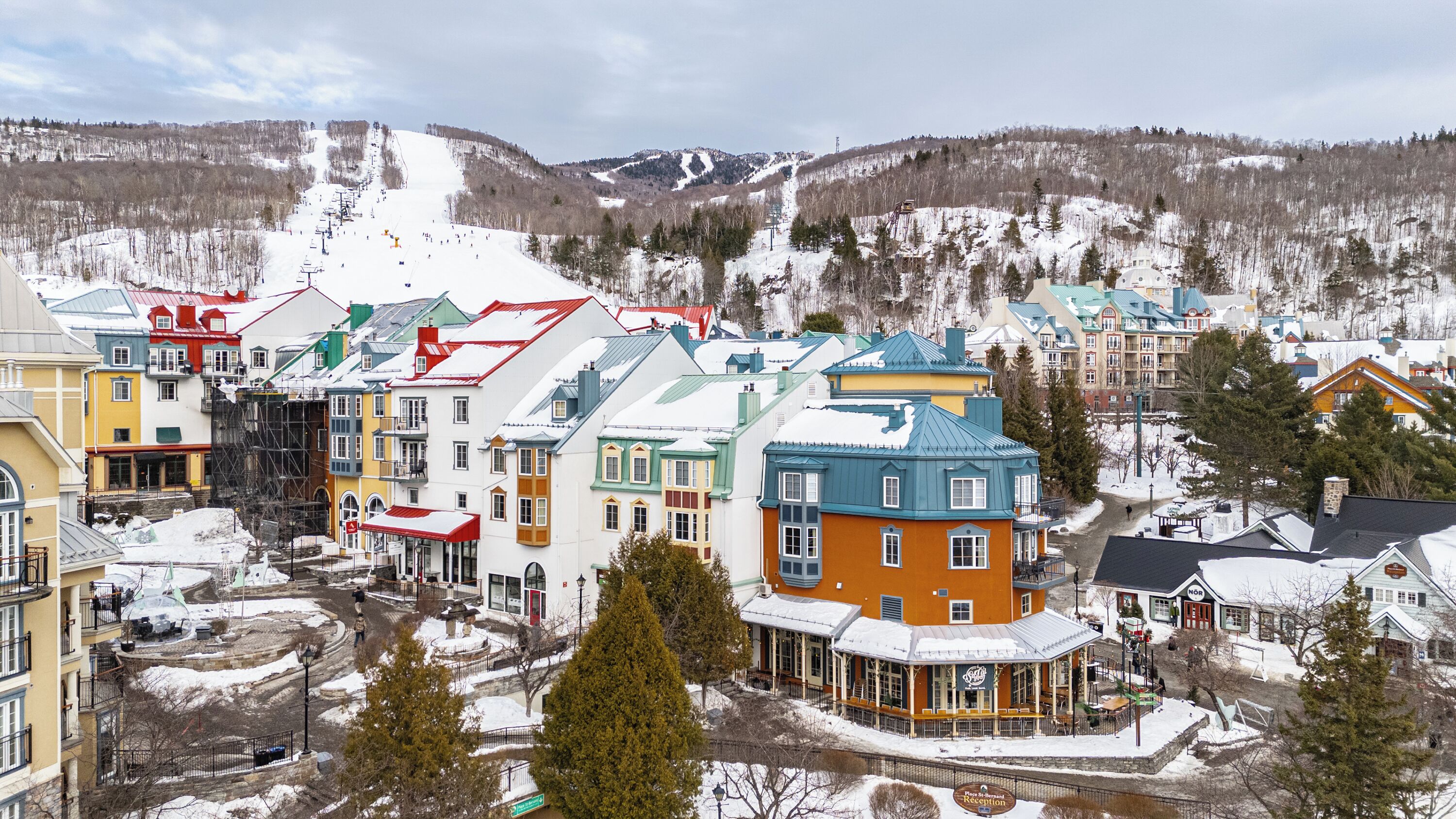 Un pueblo cubierto de nieve con edificios coloridos, un telesilla y una montaña al fondo.