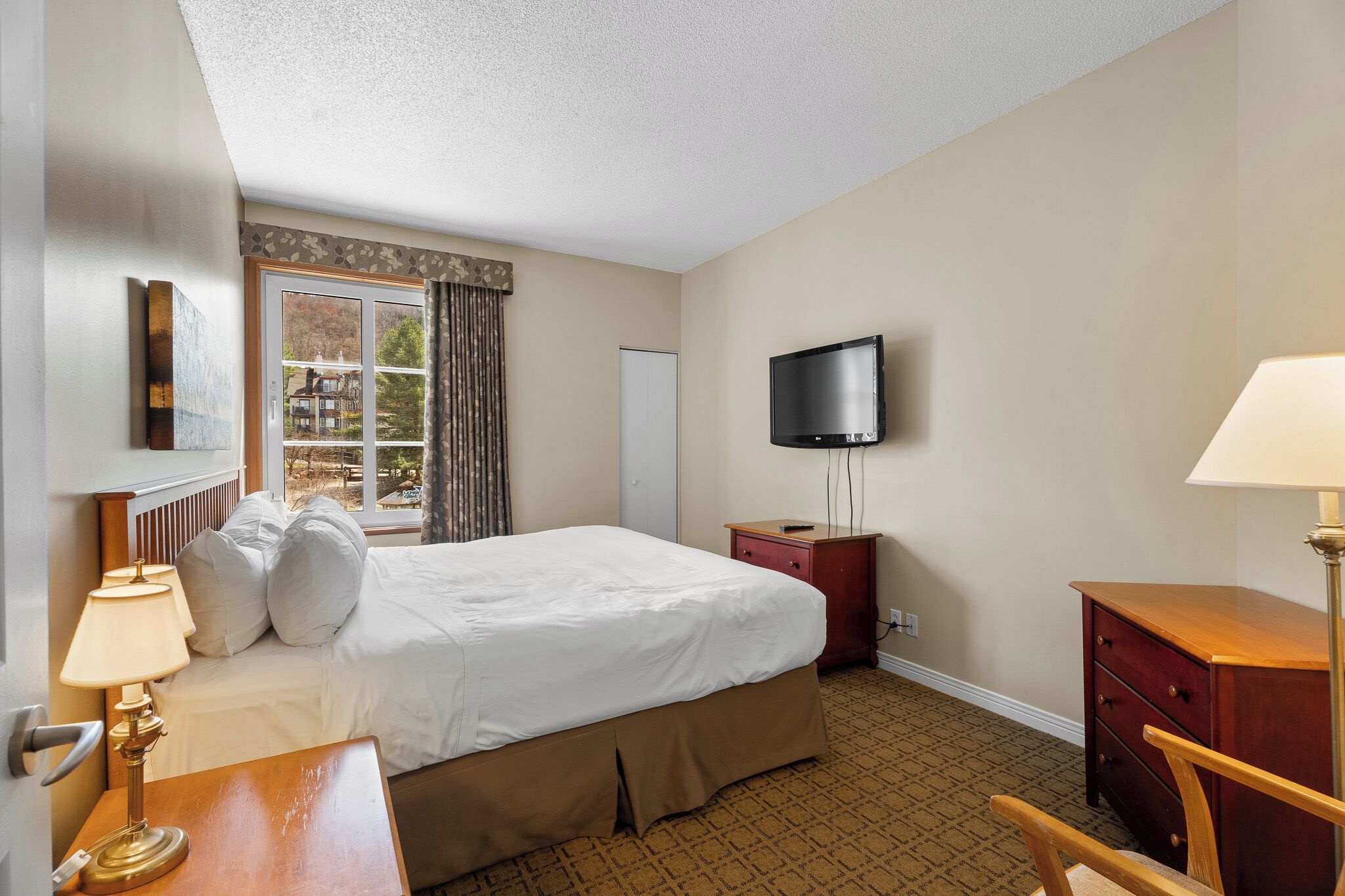 A hotel room with a bed, a desk, a chair, a television, and a window with curtains.