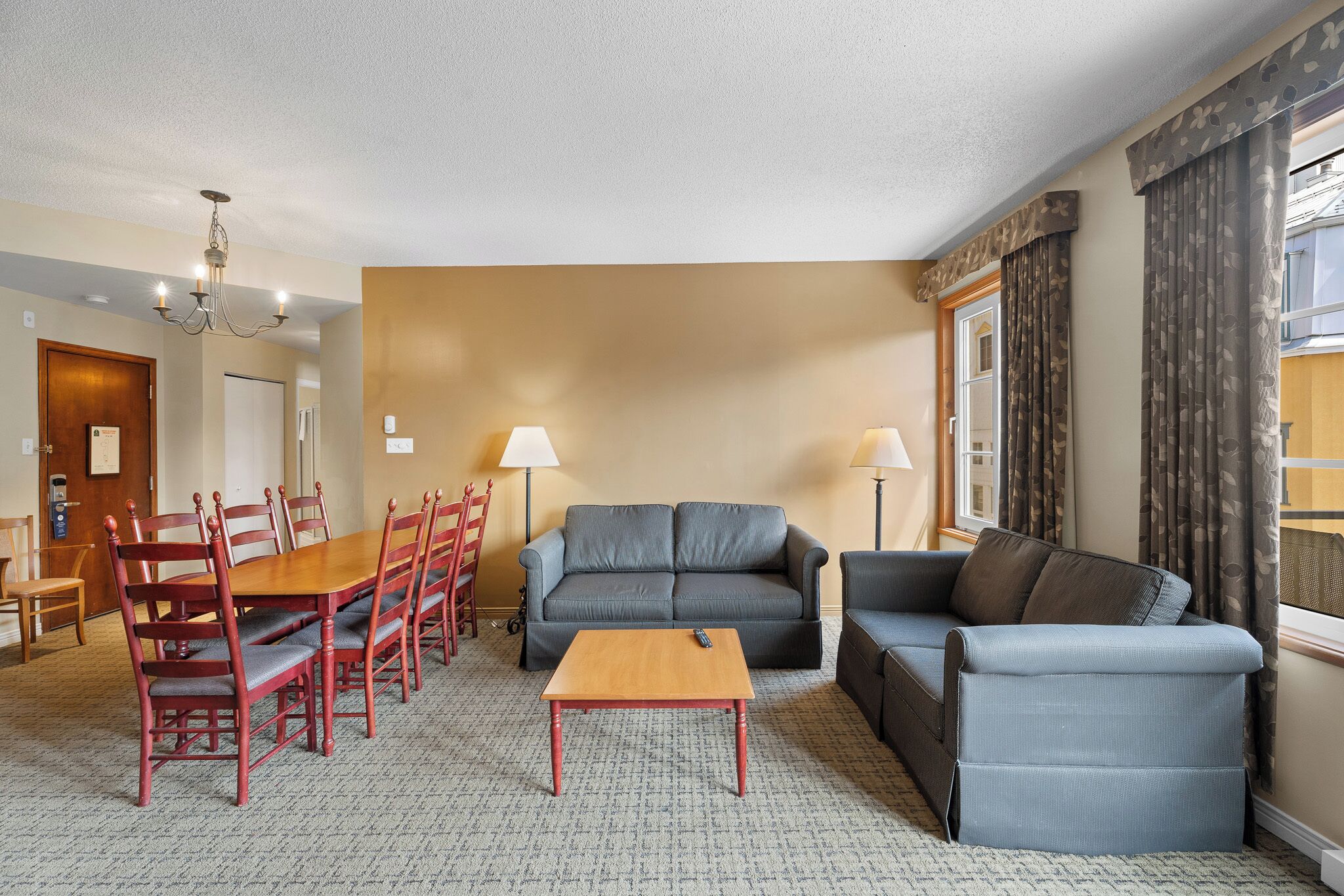 A hotel room with a dining table, chairs, a sofa, a loveseat, a coffee table, and two lamps.