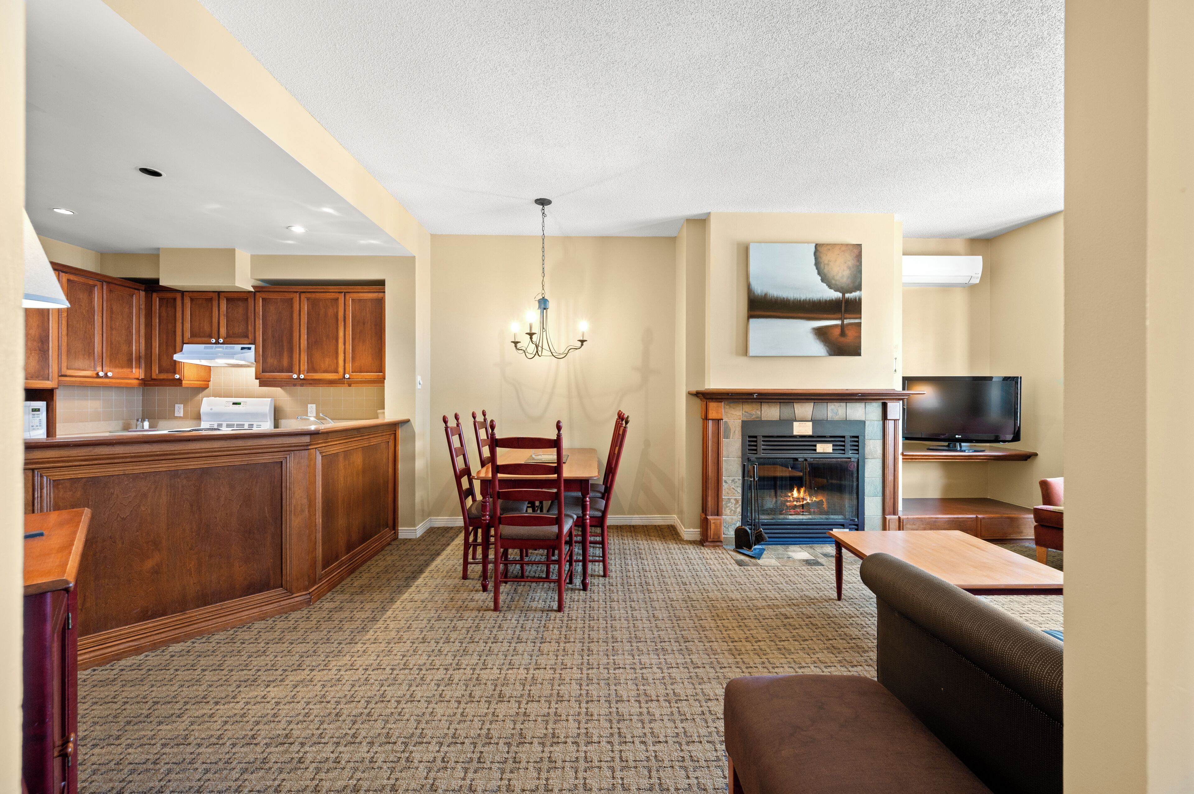 A spacious living area with a fireplace, a dining table with chairs, a kitchen with wooden cabinets, and a television on a stand.