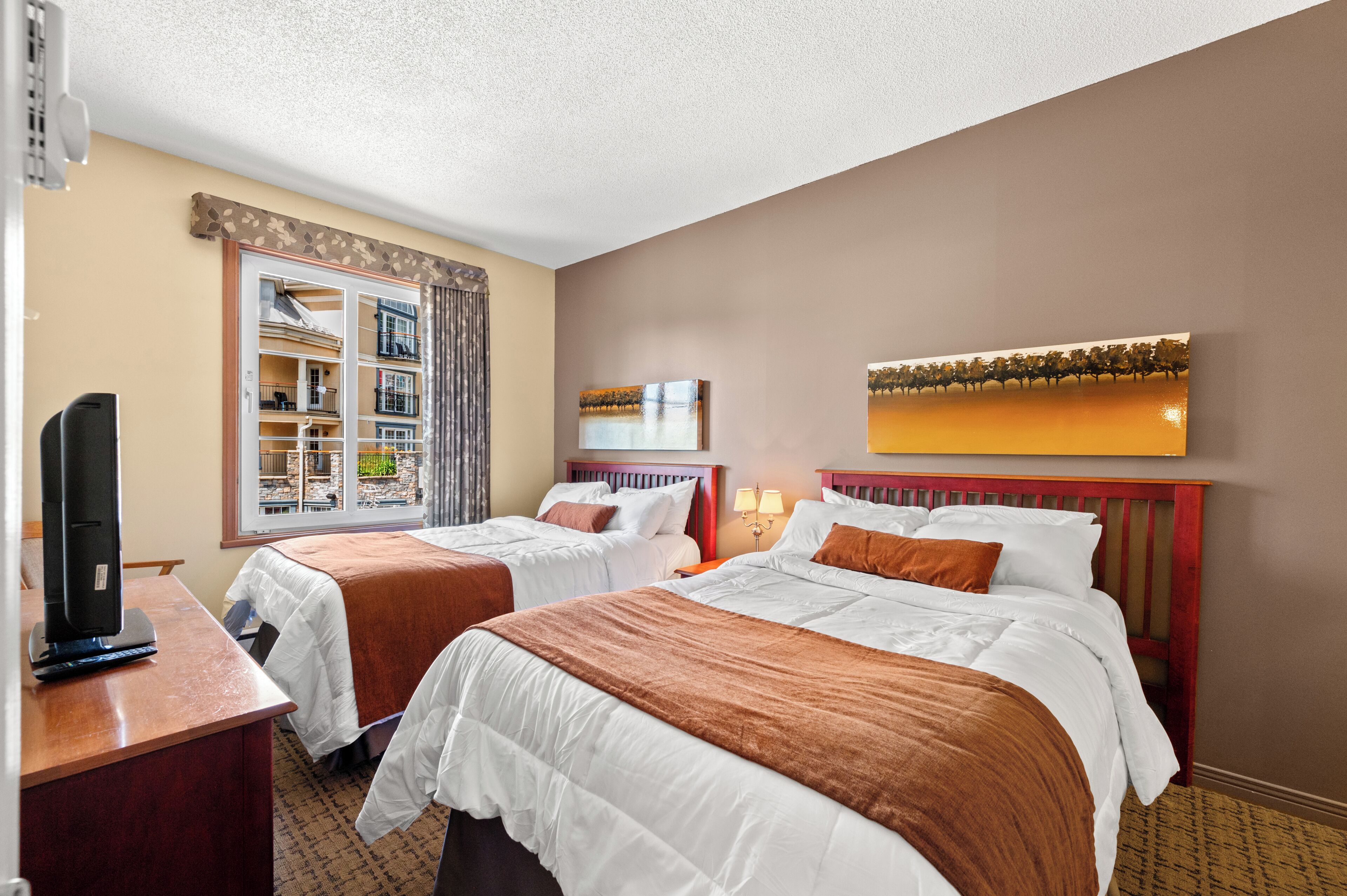 A hotel room with two beds, a television, a bookshelf, and a painting on the wall.