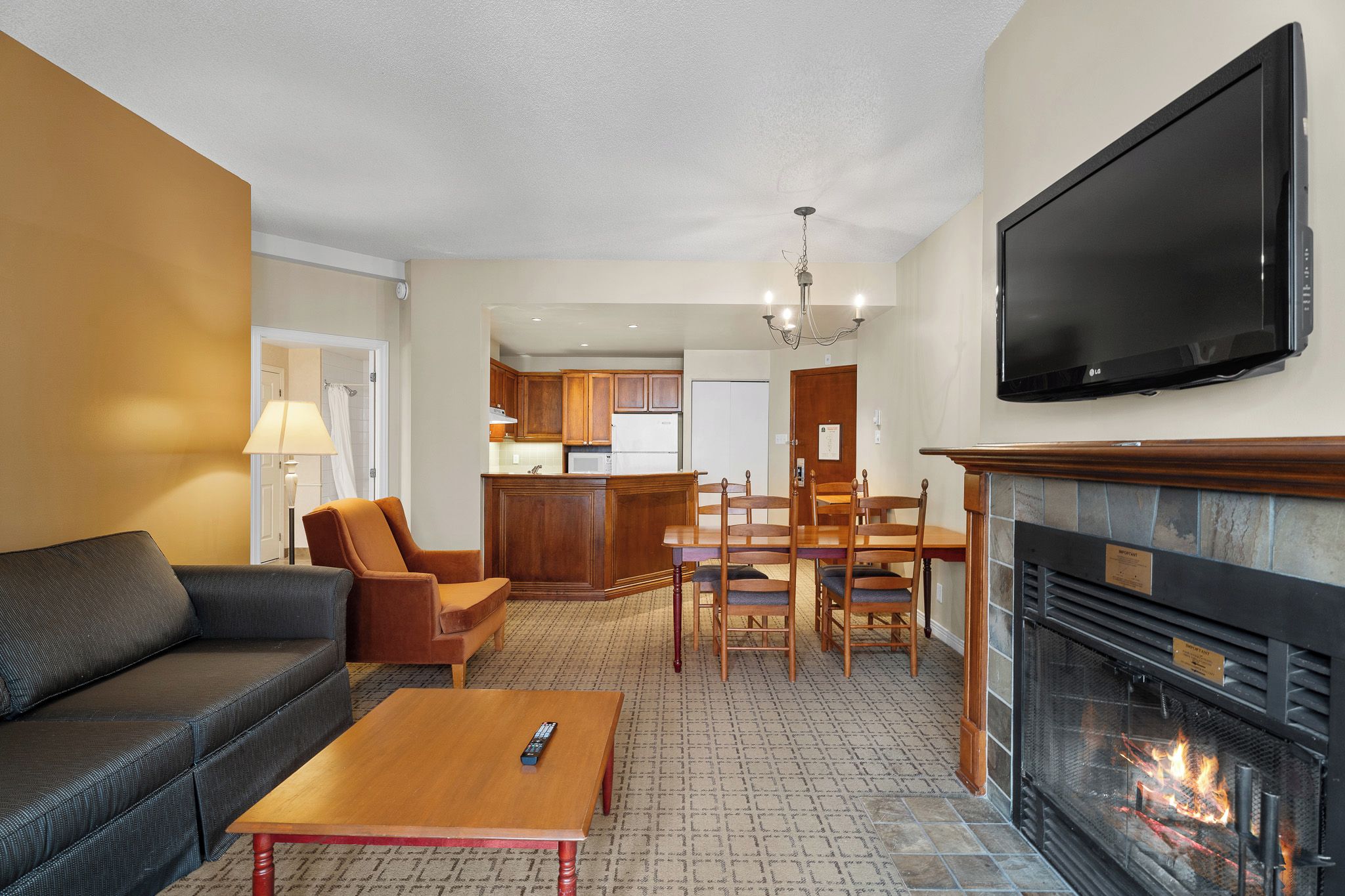 A living room with a sofa, armchair, coffee table, fireplace, TV, kitchen area, and dining table.