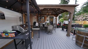 Une terrasse extérieure équipée d’un barbecue, de sièges et de guirlandes lumineuses.
