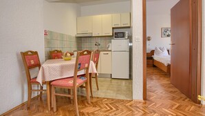 Cocina compacta con electrodomésticos básicos, comedor con dos sillas y una mesa, y dormitorio con cama y mesita de noche.