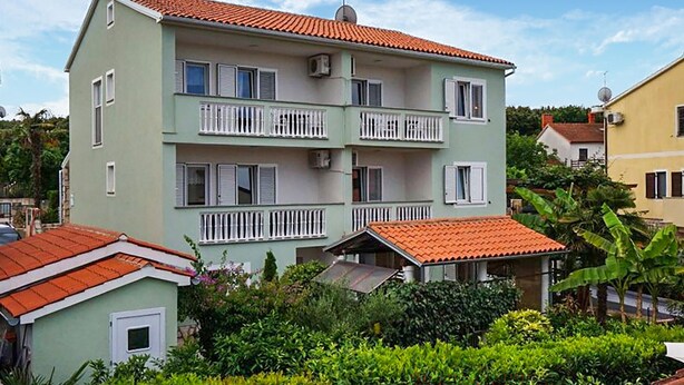 Un edificio de varios pisos con balcones, techo de tejas rojas y un área ajardinada.