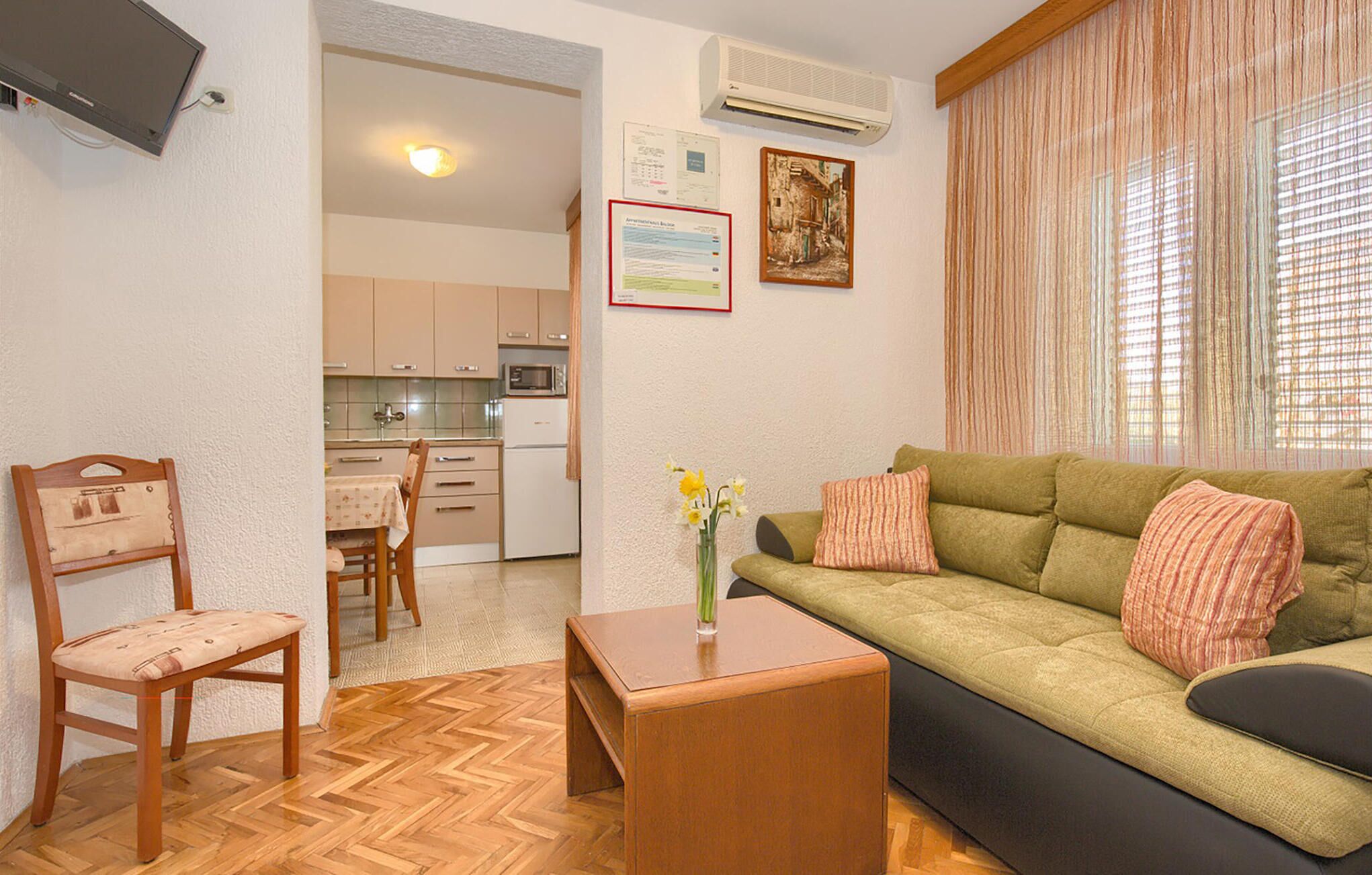 Una sala de estar con sofá, una silla de madera, una mesita y una cocina al fondo.