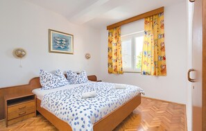 A bedroom with a wooden bed, a nightstand, a wall-mounted fan, a window with curtains, and a framed picture on the wall. - Cozy apartment in Pula with WiFi (Pula)