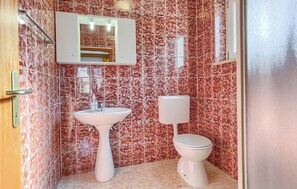 Ein Badezimmer mit einem Standwaschbecken, einer Toilette und einem Spiegel über dem Waschbecken.