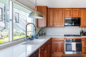 A modern kitchen with wooden cabinets, stainless steel appliances, a large window, and a pendant light. - Water and Mountain Views, 2 Kitchens, 2 Decks, Sunny Hilltop Retreat, Sleeps 11 (Seattle)