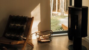 Una habitación acogedora con un ventanal grande, una silla de mimbre, una mesita y un estufa de leña.