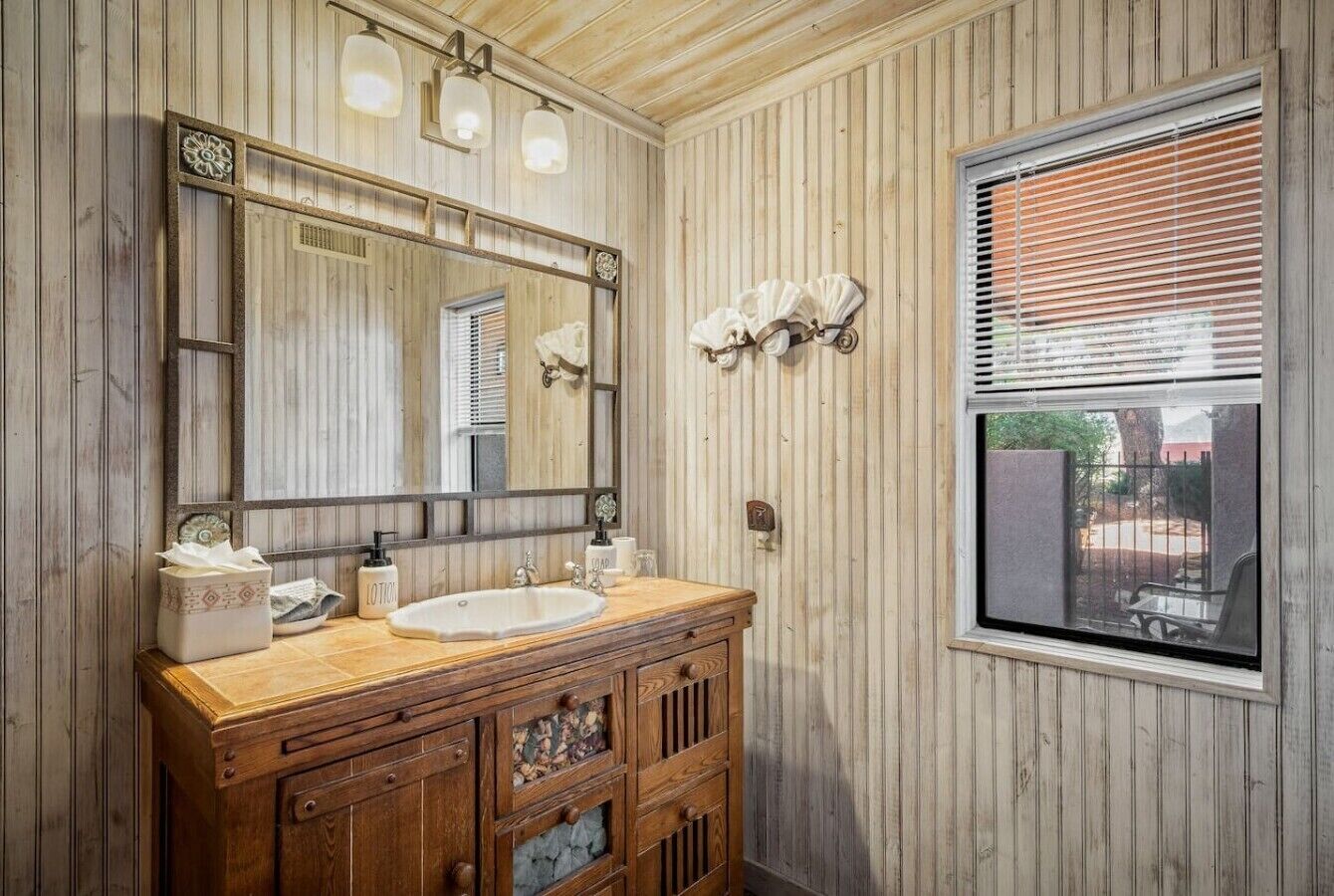 A bathroom with wooden paneling, a large mirror, a sink, and a window with blinds.
