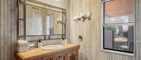 A bathroom with wooden paneling, a large mirror, a sink, and a window with blinds.
