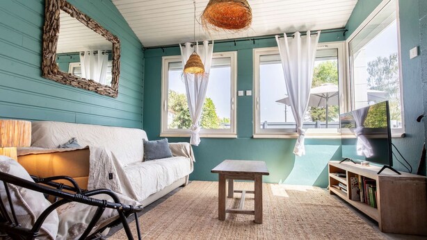 Een gezellige kamer met een witte bank, een klein houten tafeltje, een hanglamp van riet en een spiegel aan de muur.