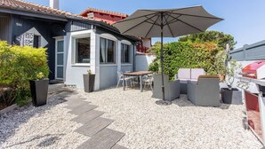 Een terras met buitenmeubilair, een barbecue en een huis met pannendak.