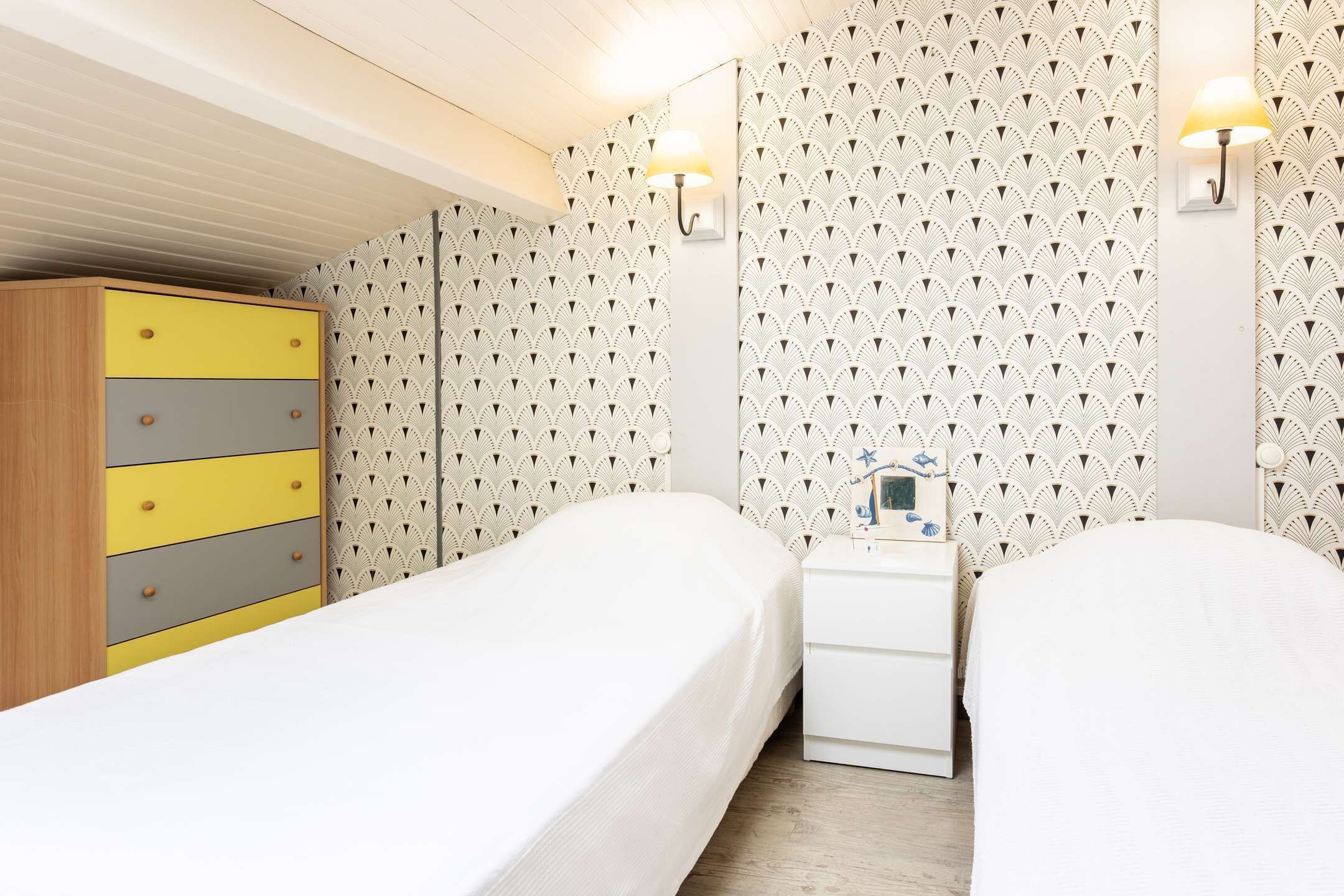 Une chambre avec deux lits simples, une table de chevet avec une lampe et une armoire avec des tiroirs.