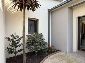 Ein Gebäude mit Fenster, Tür und einem kleinen Garten mit Pflanzen und einem Baum.