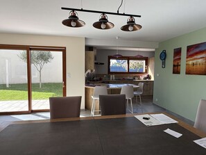 Eine moderne Küche mit Essbereich, großen Fenstern und einer Glastür, die in einen Garten führt.