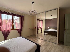 Ein Schlafzimmer mit Bett, Schiebbettwäscheschrank und einem Fenster mit Vorhängen.