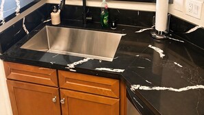 Een moderne keuken met een zwarte marmeren aanrecht, een roestvrijstalen spoelbak, houten kastjes en een potplantje op de vensterbank.