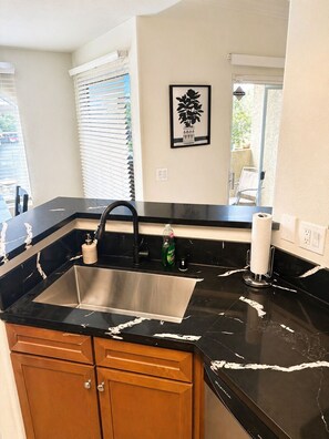 A modern kitchen with a black marble countertop, stainless steel sink, wooden cabinets, and a potted plant on the windowsill. - Spacious 3-bedroom condo with UNREAL views near Strip with all the amenities!!! (Las Vegas)