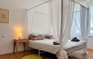 A bedroom with a canopy bed, a bedside table with a lamp, and a green rug.