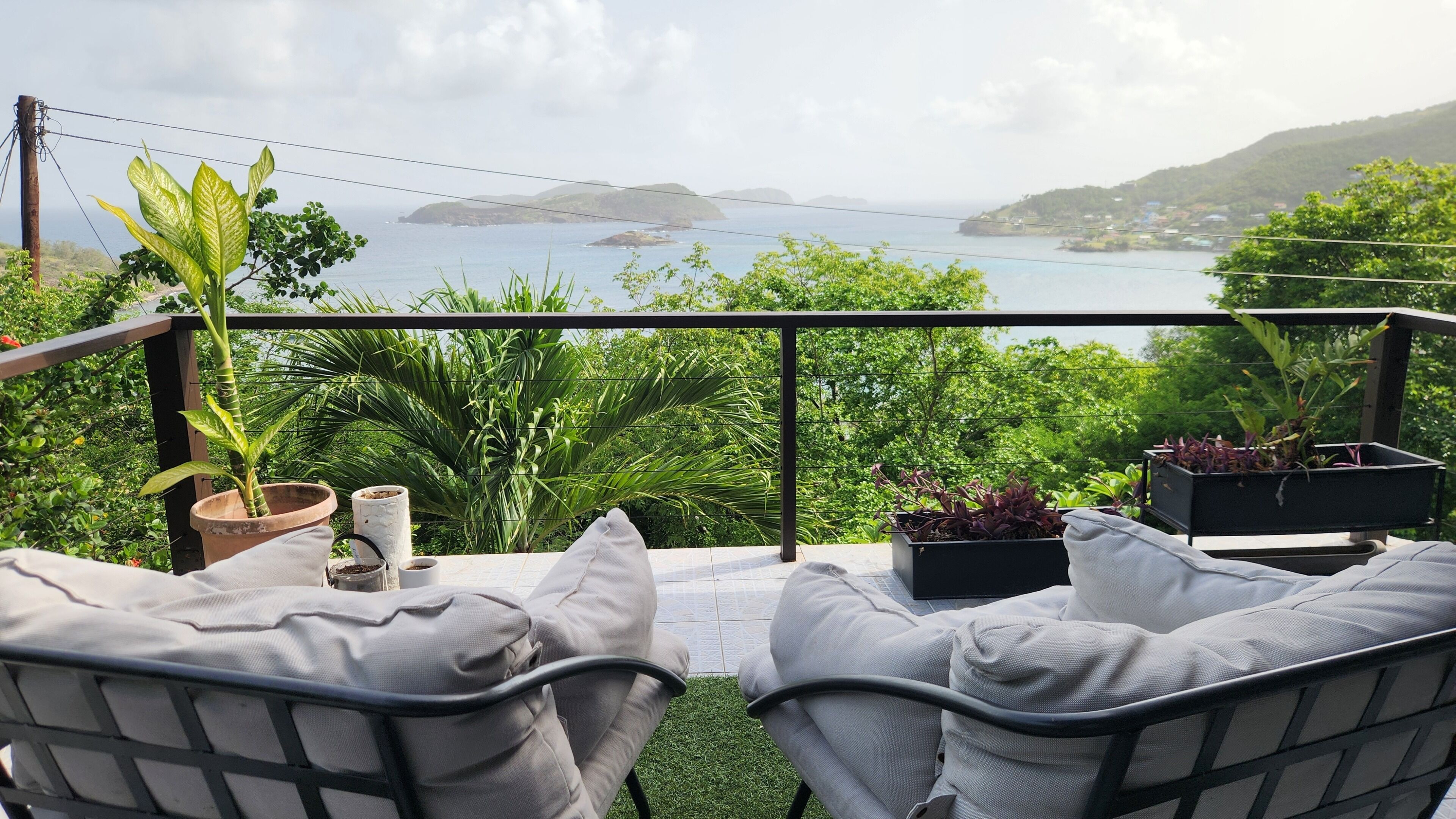 Ein Balkon mit zwei Stühlen, Blumentöpfen und Blick auf das Meer und die Hügel.